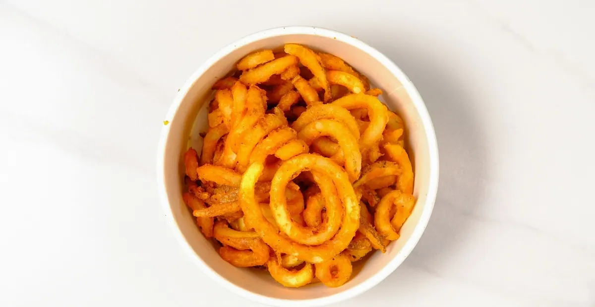 Seasoned curly fries in a paper bowl
