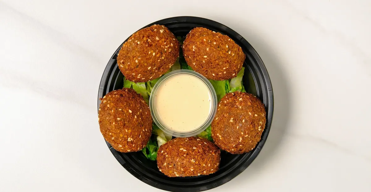 Five falafel on greens around a cup of tahini sauce